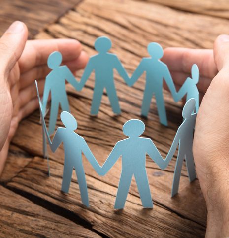 Cropped image of businessman's hands covering paper team on wooden table
