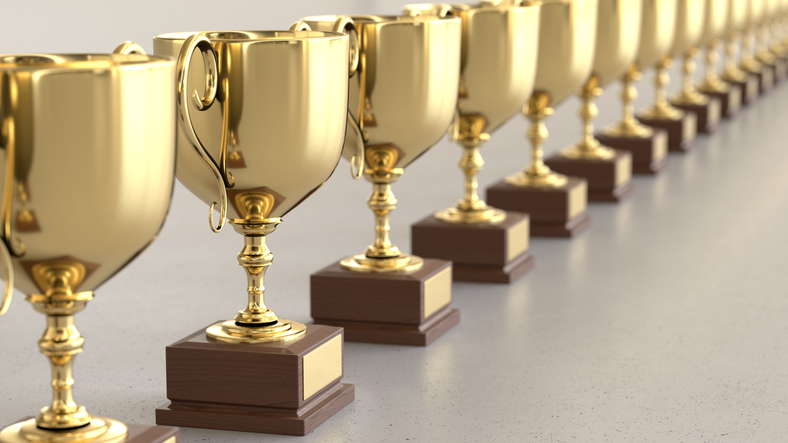 Line of Gold Trophys on a simple light surface. This image is a 3d render.