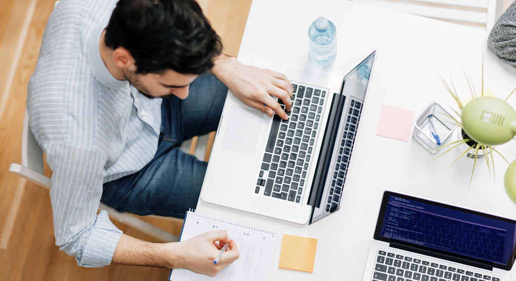 man sitting at laptop writing notes