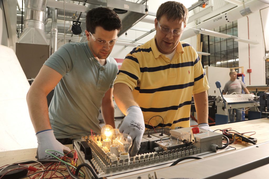 Two menu inspecting electrical panel with light bulbs