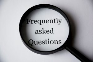 A white sheet of paper with Frequently asked Questions written on it and a magnifying glass laying on the paper to magnify the words Frequently asked Questions.