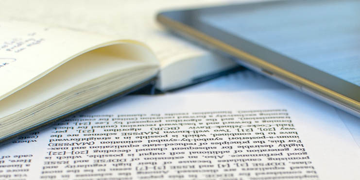 Photo of open books, typewritten pages and the corner of a laptop or ipad.